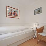 A bedroom with bed, chair, and wall pictures.
