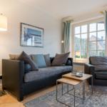 Living room with sofa, armchair, table, and windows with curtains.