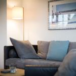 A sofa with cushions and a floor lamp on the wall.