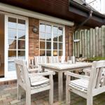 Terrace with wooden table and chairs, view into house through glass doors.