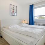 Bedroom with white bed, blue curtains, and window view.
