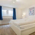 Bedroom with white bed, blue curtains, and wooden floor.