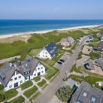 Houses near the beach with dunes and sea in the background.