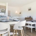 Dining area with white table and chairs, next to living area with gray sofa.