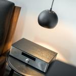 Schwarze Lampe hängt über einen Tisch mit Audio-Gerät und Bett.
