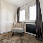 Zimmer mit weißen Schränken, Sessel und Fenstern mit Vorhängen.