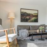 Ein Wohnzimmer mit grauem Sofa, Holzstuhl und Wandbild.
