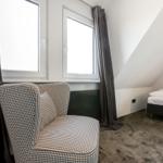 Schlafzimmer mit Dachschräge, Bett und Sessel mit kariertem Stoff.