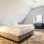Schlafzimmer mit Doppelbett, Sessel und Fenster unter Dachschrägen.