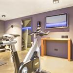 Fitnessraum mit Fahrradtrainer, Dumbbells und Fernseher an der Wand.