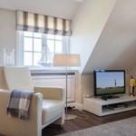 A living room with a chair, TV, and windows under a sloped ceiling.