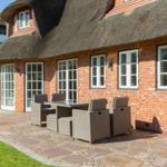 Rostrote Ziegelmauer mit strohgedecktem Dach und Terrasse mit Sitzgruppe.