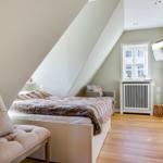 Schlafzimmer mit Dachschrägen, Bett, Sessel und Fenster.