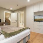 Schlafzimmer mit Bett, TV und Stuhl. Tür führt zur Badewanne und Treppe.