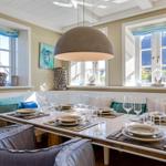Esszimmer mit Tisch, Stühlen und Fenstern mit blauen Vorhängen.