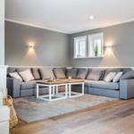 A living room with gray sofa, wooden floor, and two windows on the wall.