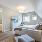 Bedroom with sloped ceiling, bed, TV, and view into bathroom