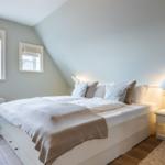 Bedroom with sloped ceiling, bed, nightstand, and windows.