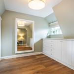 Bedroom with wooden floor, white closet, and mirror. Window with roller blind.