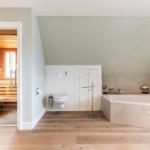 Bathroom with bathtub, toilet, and sauna. Wooden floor and light gray walls.