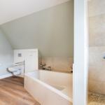 Bathroom with bathtub, shower, and toilet under sloped ceiling