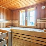 Sauna with wooden bench, window, and thermometer on the wall.