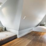 Room with sloped ceilings, two beds, and hardwood floor.