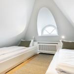 Two single beds under sloped ceilings with window and radiator.