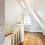 Staircase with wooden floor, arched window, and wallpaper with sea creature motifs.