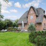 Red brick house with thatched roof, garden with sun loungers and flower beds.