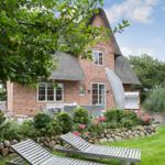 Red brick house with thatched roof, garden with lounge chairs and flower beds.