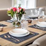 Dining table with placemats, plates, and glasses. A vase with flowers is in the center.
