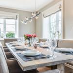 Dining room with long table, chairs, and windows. Table set with dishes and flowers.