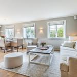 Living and dining area with sofa, table and chairs. Wooden floor and windows with view outside.