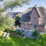 Red brick house with thatched roof, garden with sun loungers and terrace.