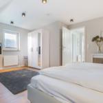 Schlafzimmer mit Doppelbett, Schrank und Fenster. Wandbild und Teppich sichtbar.