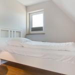 Ein Schlafzimmer mit weißem Bett, Fenster und schwarzem Hängelampen.