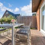 Terrasse mit Tisch und Stühlen, gepflastert, mit Blick auf einen Garten und Zaun.