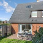 Haus mit Terrasse, Garten und Sitzgelegenheit. Rotes Mauerwerk und grauer Dachfirst.