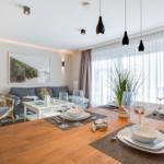 Esszimmer mit Holztisch, Stühlen und Glastisch. Sofa, Wandbild und Fenster mit Vorhängen.