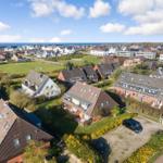 Village with houses and green areas by the sea under blue sky.