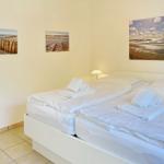 Room with double bed, white linens, and beach pictures on the walls.