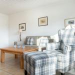 Living room with sofa, armchair, and table. Wall art and window visible.