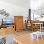 Living room with dining area and kitchen. Wooden furniture, TV, and kitchen visible.