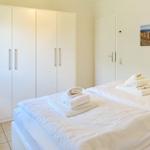 Two beds with white sheets and folded towels. Background: white wardrobe and wall picture.