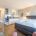 Bedroom with kitchenette and dining area. Wooden floor and modern furnishings.