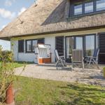 Haus mit Strohdach, Terrasse mit Liegestühlen und Strandkorb.
