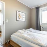 Schlafzimmer mit Bett, Fenster und Bild an der Wand. Durchgang zu einem Raum mit Stuhl.