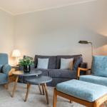 Wohnzimmer mit Sofa, zwei Sesseln und Tisch. Wandbild und Beleuchtung sichtbar.