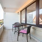 Terrasse mit Tisch und zwei Stühlen mit pinken Kissen. Blick auf Dächer und Grünflächen.